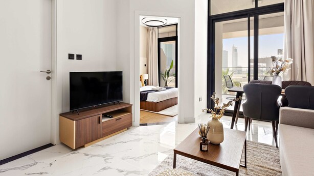 Habitación de hotel moderna con un televisor grande, un armario de madera, una cama y un balcón con vistas a la ciudad.