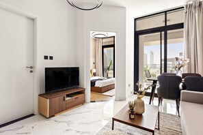 A modern hotel room with a large TV, a wooden cabinet, a bed, and a balcony with a view of the city. - Silkhaus 1bdr in Al Maryah Vista Near Al Reem (Abu Dhabi)