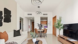 A modern living room with a sofa, coffee table, and a TV on a wooden stand. There is a dining area with a table and chairs in the background. - Silkhaus 1bdr Near Reem Park at Julphar Tower (Abu Dhabi)