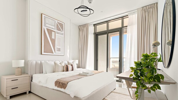 A modern bedroom with a large bed, a nightstand, a desk with a plant, and a large window with curtains. - Silkhaus 1bdr Near Reem Park at Julphar Tower (Abu Dhabi)