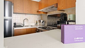 A modern kitchen with wooden cabinets, a stainless steel refrigerator, a gas stove, and a coffee maker. - Silkhaus 1bdr Near Reem Park at Julphar Tower (Abu Dhabi)