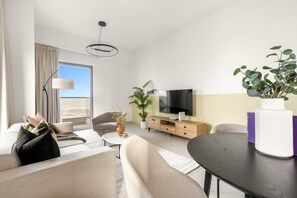 A modern living room with a sofa, armchair, coffee table, and a TV on a wooden cabinet. - Silkhaus Cityscape 1BR Najmat (Abu Dhabi)