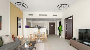 A modern living room with a sofa, coffee table, and TV stand. There is a dining area with a table and chairs. The room has a neutral color palette and modern decor. - Silkhaus Signature 1bdr Najmat Al Reem Island (Abu Dhabi)