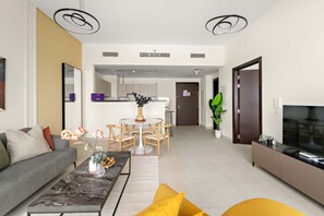 A modern living room with a sofa, coffee table, and TV stand. There is a dining area with a table and chairs. The room has a neutral color palette and modern decor. - Silkhaus Signature 1bdr Najmat Al Reem Island (Abu Dhabi)