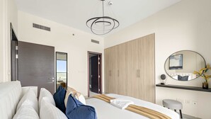 A modern bedroom with a large bed, a wardrobe, a mirror, and a ceiling light fixture. - Silkhaus Signature 1bdr Najmat Al Reem Island (Abu Dhabi)