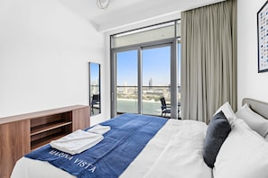 A hotel room with a bed, a view of the city, a balcony, and a desk with a chair. - Silkhaus Elite 2bdr Marina Vista Sea View (Dubai)