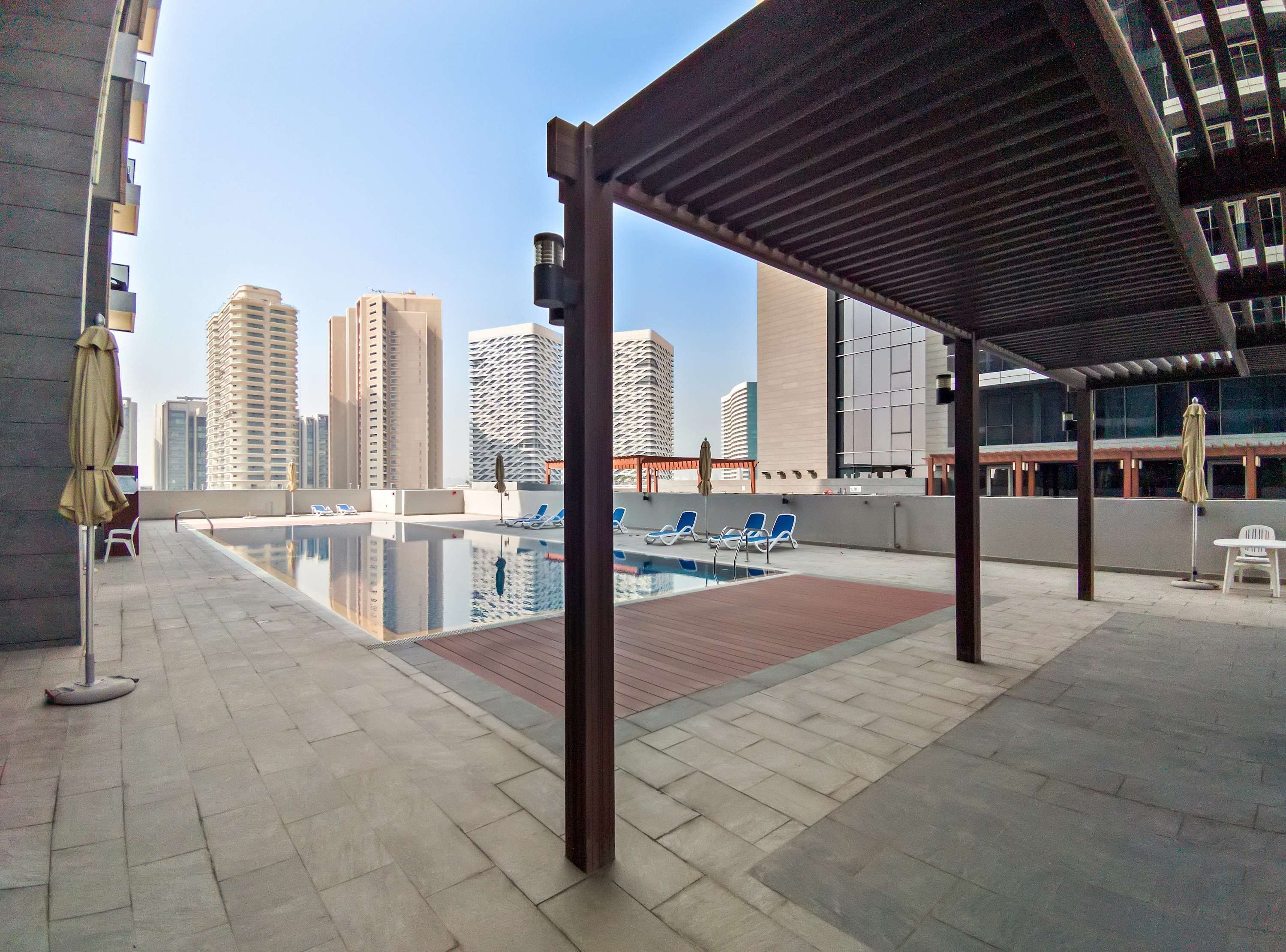 A rooftop pool area with a view of tall buildings, lounge chairs, and umbrellas. - Silkhaus Comfy 1bdr Najmat Tower in Reem Island (Abu Dhabi)
