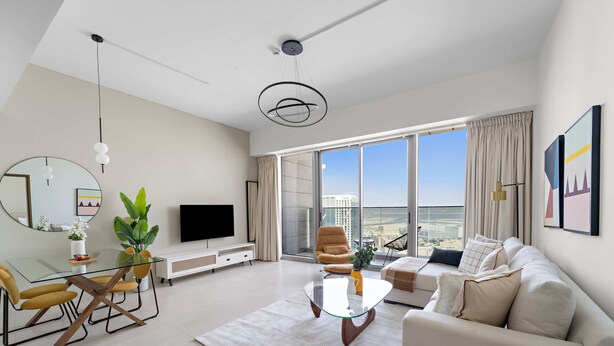 A modern living room with a glass coffee table, a sofa, a dining area with yellow chairs, a large window with a city view, and a flat-screen TV. - Silkhaus Comfy 1bdr Najmat Tower in Reem Island (Abu Dhabi)