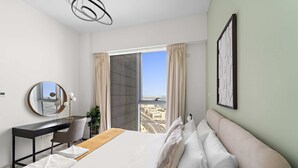 A hotel room with a bed, a desk, a chair, a large window with curtains, and a view of the city. - Silkhaus Comfy 1bdr Najmat Tower in Reem Island (Abu Dhabi)