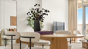 Un espace repas moderne avec une table ronde en bois, des chaises blanches et un vase contenant des feuillages noirs et blancs.