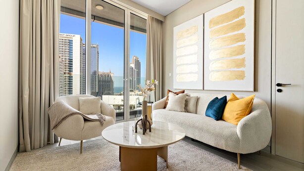 A modern living room with a large window, a round coffee table, and a sofa with decorative pillows. - Silkhaus Luxury 1BR Marina Star Dubai Marina (Dubai)