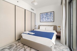 Hotellihuone, jossa on suuri sänky, vaatekaappi, yöpöytä, lamppu ja ikkuna, jossa on verhot.