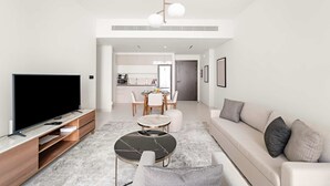 A modern living room with a flat-screen TV, a round coffee table, a sofa, and a dining area with a table and chairs. - Silkhaus 1bdr Marina Vista Private Beach (Dubai)