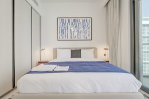 A modern hotel room with a large bed, a city view, a framed abstract painting, and bedside lamps. - Silkhaus Elegant 1bdr Sea View Private Beach (Dubai)
