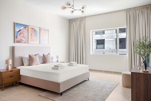 A modern bedroom with a large bed, a nightstand, a bedside table, a window with curtains, and framed pictures on the wall. - Silkhaus Cozy 1bdr Retreat Dubai Marina (Dubai)