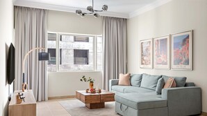En moderne stue med en grå sofa, et træbord, et fjernsyn og et stort vindue med gardiner.