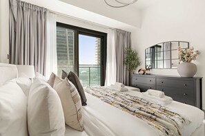 A modern hotel room with a large bed, grey curtains, a mirror, a dresser, and a balcony view. - Silkhaus Modern 2BR Merano Tower in Business Bay (Dubai)