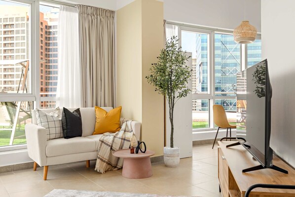 A modern living room with a sofa, coffee table, TV, and a large window with curtains. - Silkhaus Large Studio Madison Res High Floor (Dubai)