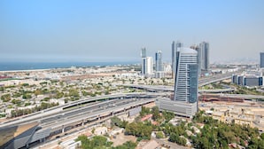 Ein Hochhaus mit modernem Design, umgeben von einer Stadtlandschaft mit weiteren Hochhäusern und einer Autobahn.