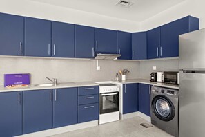 A modern kitchen with blue cabinets, a stainless steel refrigerator, a built-in oven, and a washing machine. - Silkhaus Large Studio Madison Res High Floor (Dubai)