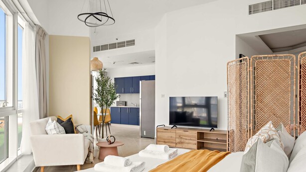 Ein modernes Hotelzimmer mit einem großen Bett, einem Fernseher, einem Holzschrank und Blick auf die Küche sowie den Balkon.