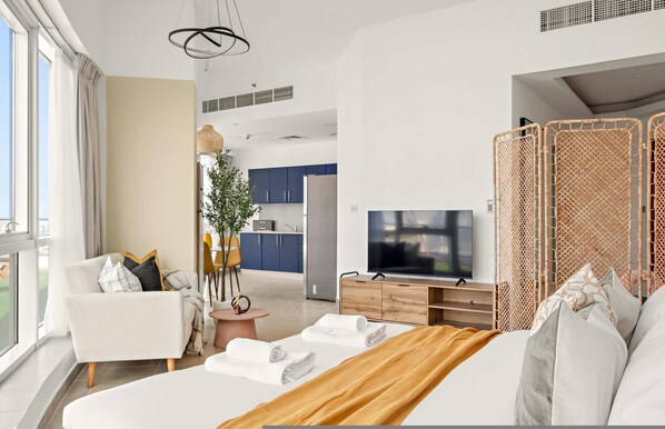 A modern hotel room with a large bed, a TV, a wooden cabinet, and a view of the kitchen and balcony. - Silkhaus Large Studio Madison Res High Floor (Dubai)