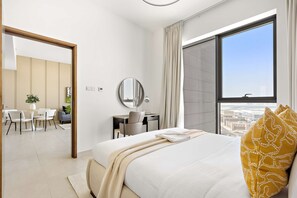 Ett modernt hotellrum med ett stort fönster, en säng med en vit och gulmönstrad kudde, en rund spegel och ett skrivbord med en stol.