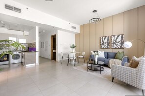 A modern living room with a sofa, coffee table, and chairs. There is a kitchen area with appliances and a dining table. - Silkhaus Modern 1bdr Stay at Najmat in Reem Island (Abu Dhabi)