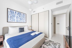 A modern hotel room with a large bed, a blue throw blanket, a framed abstract painting, a wardrobe, and a TV. - Silkhaus Chic Seaview 1bdr Marina Vista Tower (Dubai)