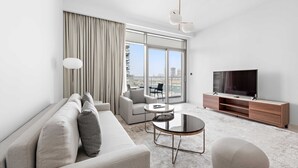 A modern living room with a sofa, a coffee table, a TV, and a large window with curtains. - Silkhaus Chic Seaview 1bdr Marina Vista Tower (Dubai)