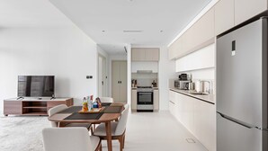 A modern kitchen with a built-in oven, microwave, and refrigerator. There is a dining area with a table and chairs, and a television on a stand. - Silkhaus Chic Seaview 1bdr Marina Vista Tower (Dubai)