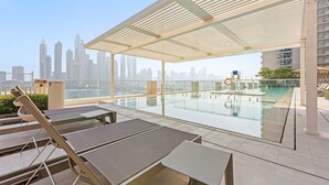 Zona de piscina en la azotea con tumbonas y barandilla de cristal con vistas al horizonte urbano.