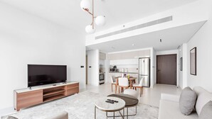 Ein modernes Wohnzimmer mit Flachbildfernseher, einer Couch, einem Couchtisch und einem Essbereich mit Küche im Hintergrund.
