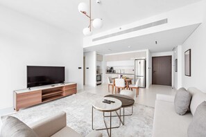 A modern living room with a flat-screen TV, a sofa, a coffee table, and a dining area with a kitchen in the background. - Silkhaus 1bdr w Private Tower Beach Marina Vista (Dubai)