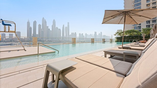 A rooftop pool area with lounge chairs and an umbrella, overlooking a city skyline. - Silkhaus 1bdr in Marina Vista Tower Private Beach (Dubai)