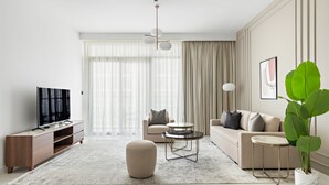 A modern living room with a sofa, ottoman, coffee table, TV, and a large plant. - Silkhaus 1bdr in Marina Vista Tower Private Beach (Dubai)