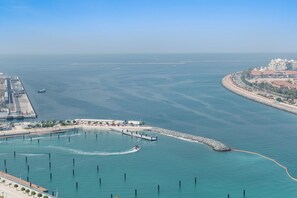 A coastal marina with a curved breakwater, a pier, and a building complex with a red roof. - Silkhaus 1bdr in Marina Vista Tower Private Beach (Dubai)