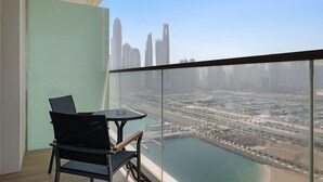 A balcony with a glass partition, a table, and two chairs, overlooking a cityscape and a body of water. - Silkhaus 1bdr in Marina Vista Tower Private Beach (Dubai)