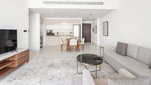 A modern living room with a TV, sofa, coffee table, and dining area. - Silkhaus 1BR in Emaar Tower With Private Pool (Dubai)