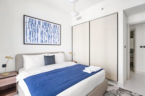 Ein modernes Hotelzimmer mit einem großen Bett, einem Nachttisch mit Lampe, einem Bilderrahmen mit einem abstrakten Gemälde und einem Kleiderschrank.