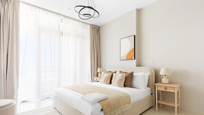 A modern hotel room with a large bed, a bedside table with a lamp, and a view of the city through large windows. - Silkhaus in Julphar Cozy 1bdr In Reem Island (Abu Dhabi)