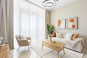 A modern living room with a white sofa, a wooden coffee table, and a large window with sheer curtains. - Silkhaus in Julphar Cozy 1bdr In Reem Island (Abu Dhabi)