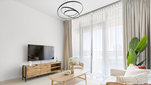 A modern living room with a flat-screen TV, wooden console, and a large plant. - Silkhaus in Julphar Cozy 1bdr In Reem Island (Abu Dhabi)