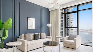 A modern living room with a sofa, two armchairs, a coffee table, and a large window offering a view of a cityscape. - Silkhaus in Marina Vista Stunning 1bdr Sea View (Dubai)