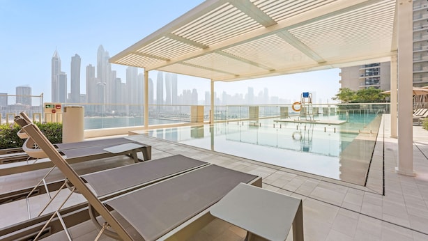 A rooftop pool area with lounge chairs, a glass railing, and a city skyline view. - Silkhaus in Marina Vista Stunning 1bdr Sea View (Dubai)