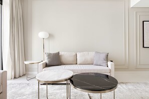 Ein modernes Wohnzimmer mit einer Couch, zwei runden Tischen, einer Stehlampe und einem gerahmten Bild an der Wand.