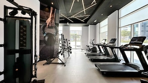 A modern gym with treadmills, weight machines, and a large mirror. - Silkhaus Cozy Studio Madison Barsha Heights (Dubai)