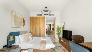 A modern hotel room with a large bed, a TV, a dining area, and a kitchen in the background. - Silkhaus Cozy Studio in Al Maryah Island (Abu Dhabi)