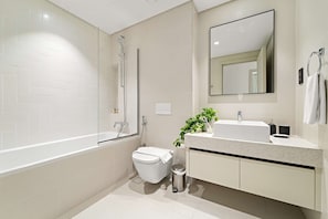 Ein modernes Badezimmer mit einer freistehenden Badewanne, einer Toilette, einem Waschbecken mit Spiegel darüber und einem Mülleimer.