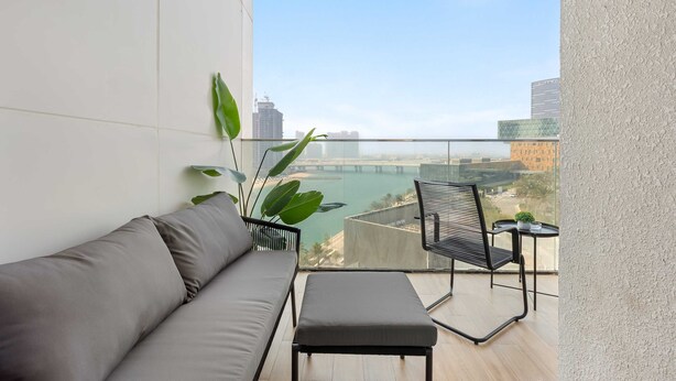 A balcony with a sofa, a small table, and a chair. - Silkhaus Elegant 1bdr Retreat Al Maryah Island (Abu Dhabi)